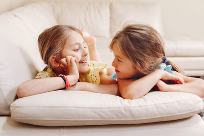 Smiling sisters talking while lying on sofa at home