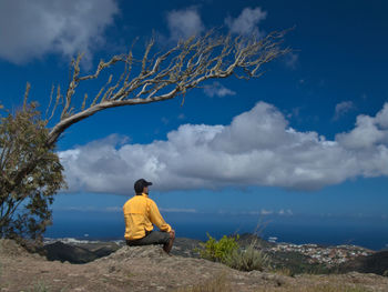 Rear view of man sitting on rock against sky