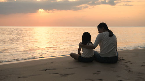 Rear view of women sitting on shore at sunset