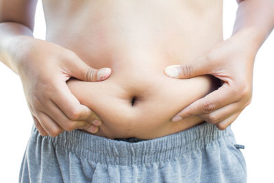 Midsection of shirtless boy pinching belly while standing against white background