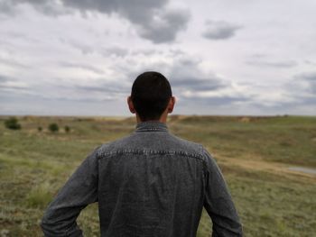 Rear view of man standing on field against sky