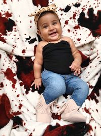 High angle portrait of smiling baby girl relaxing on blanket