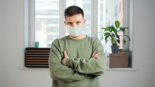 Portrait of young man standing by window at home