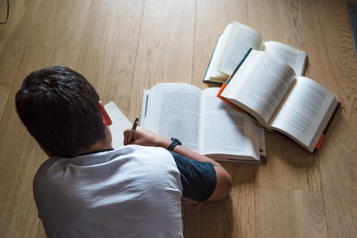 High angle view of boy studying while lying on floor at home