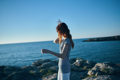 Woman standing on rock by sea against sky