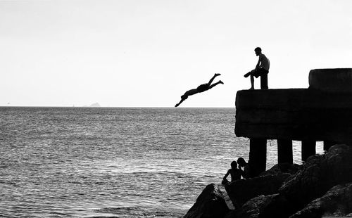 Silhouette men by sea against clear sky