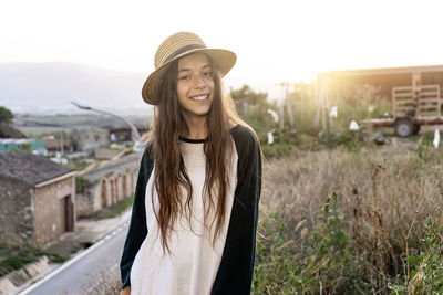 Smiling young woman wearing hat standing against building