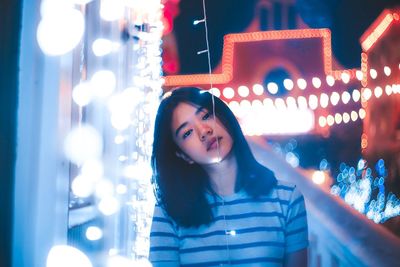 Portrait of young woman with head cocked by illuminated string lights at night