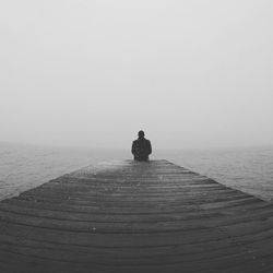 Man sitting on pier looking at sea