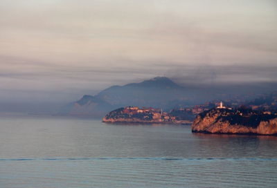 Scenic view of sea and mountain against cloudy sky