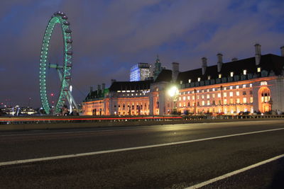 Illuminated ferris wheel in city against sky at night