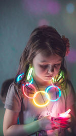 Close-up of girl wearing illuminated necklace against wall