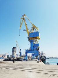 Cranes at commercial dock against clear blue sky