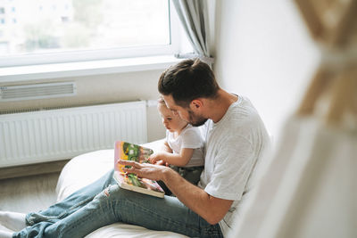 Happy father and baby girl little daughter having fun reading a book in children room at home