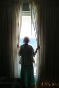 Rear view of woman looking at sea through window