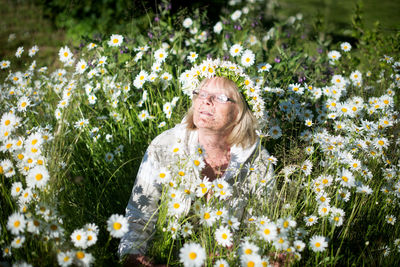 High angle view of woman wearing flowers sitting amidst daisies field