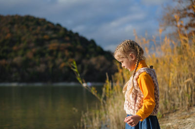 Side view of young woman standing against lake clear sunny autumn day in the forest