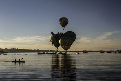 Hot air balloon flying over lake against sky during sunset
