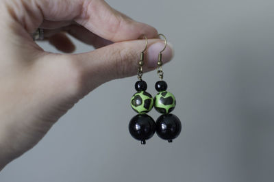 Cropped hand of woman holding earrings against gray background