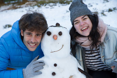 Portrait of young couple with snowman during winter