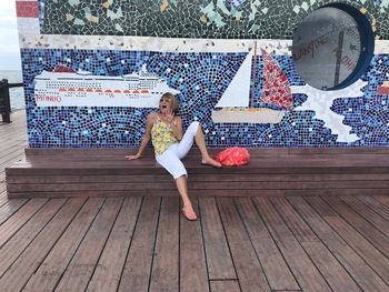 Full length of senior woman screaming while sitting against tiled wall on promenade