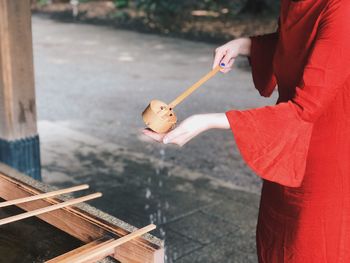 Midsection of woman pouring water using bamboo ladle while washing hand at shrine