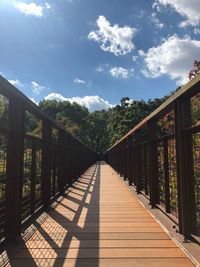 Wooden footbridge along plants and trees against sky