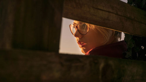 Close-up of woman wearing eyeglasses while looking away seen through hole in wood