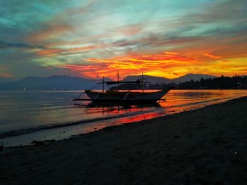 Boats moored on sea against dramatic sky during sunset