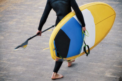 Low section of woman carrying surfboard on wooden floor