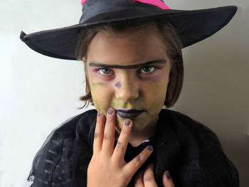Portrait of girl wearing witch costume and hat touching face standing against wall at halloween