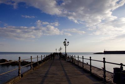 Empty jetty leading to sea against cloudy sky