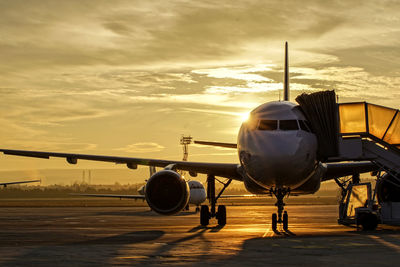 Airplane on runway against sky during sunset