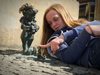 Young woman looking at statue while lying on street in city