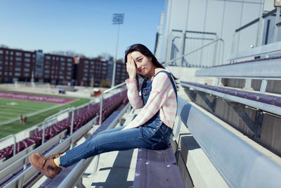 Side view portrait of young woman sitting at stadium