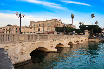 Arch bridge over river against cloudy sky