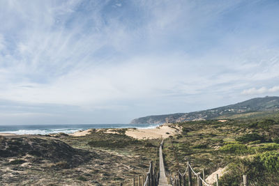 Empty, wooden boardwalk on a beach praia do guincho in sintra. view of grass and sand with hills