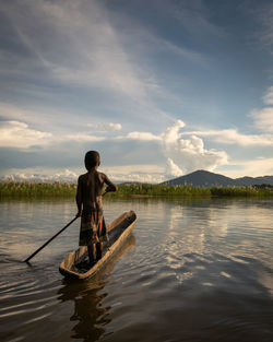 Rear view of man on boat in lake against sky