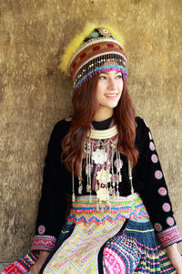 Smiling woman in traditional clothing looking away against wall