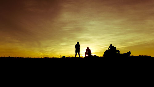 Silhouette men on landscape against sky during sunset