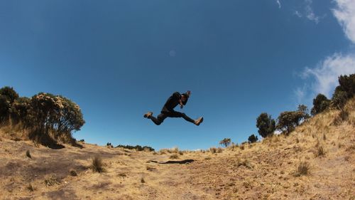 Low angle view of man jumping on mountain against sky