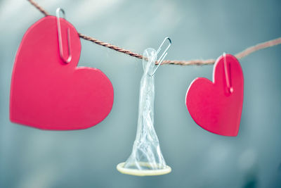 Close-up of condom with heart shape papers hanging on string