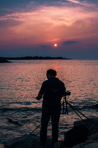 Rear view of silhouette man fishing in sea against sunset sky