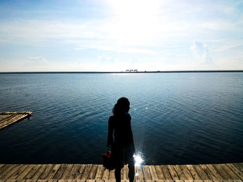 Rear view of man sitting on pier over sea against sky