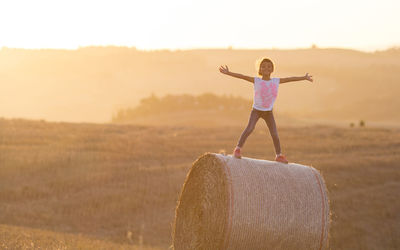 Full length of girl standing on hay bale