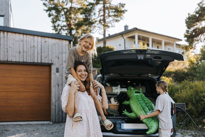 Happy mother carrying son on shoulders with boy loading crocodile float in car trunk