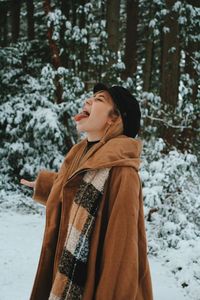 Woman sticking out tongue while standing on snow covered land