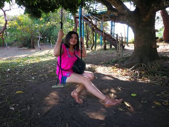 Full length portrait of happy woman sitting on tree trunk