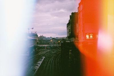 Railroad tracks by buildings in city against sky during sunset