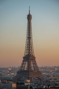 Communications tower in city against sky during sunset